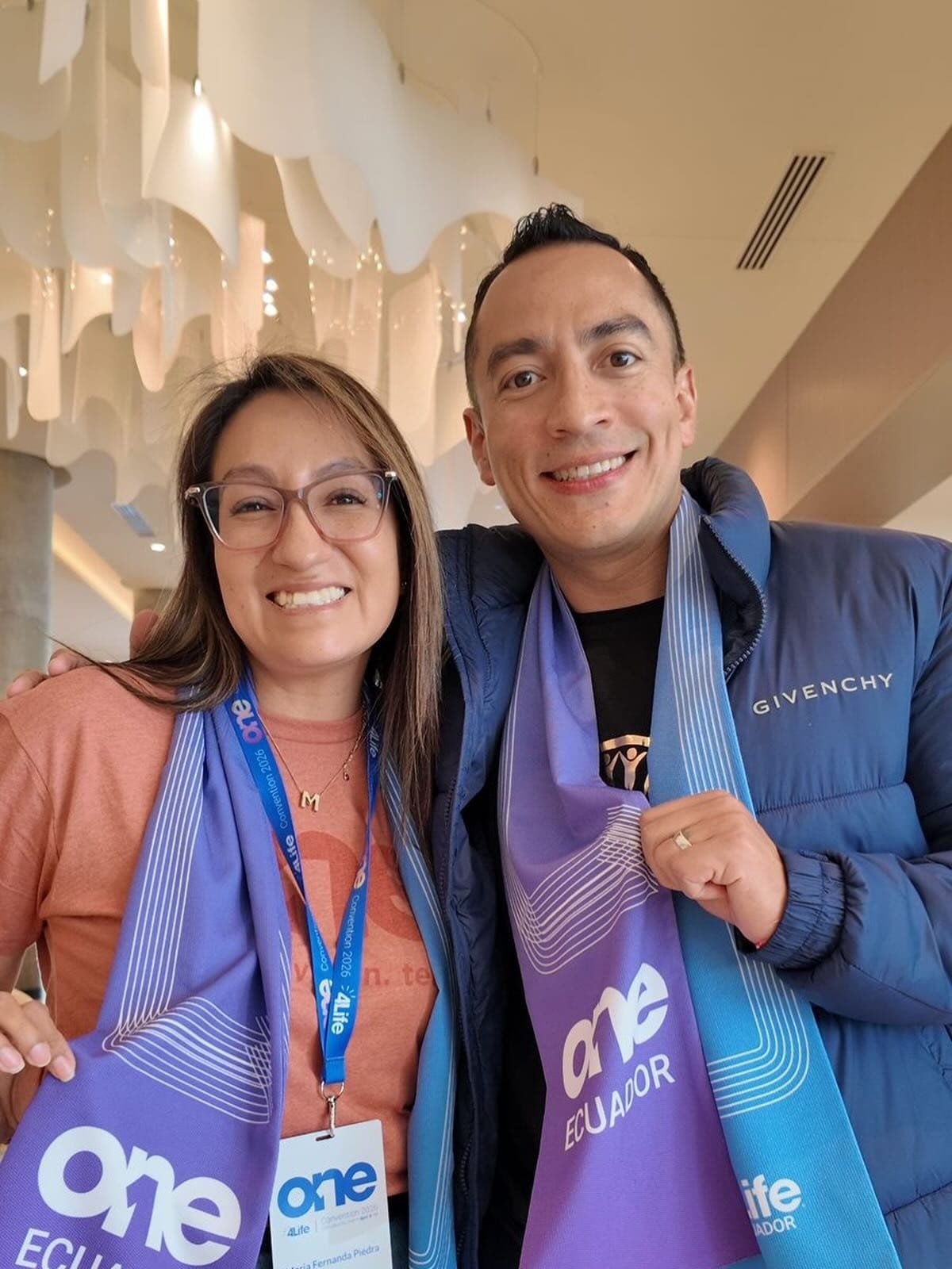 Evento de Logros 4Life - Mujer y hombre con lanyards de evento en interior elegante - Equipo de Mentoría Global